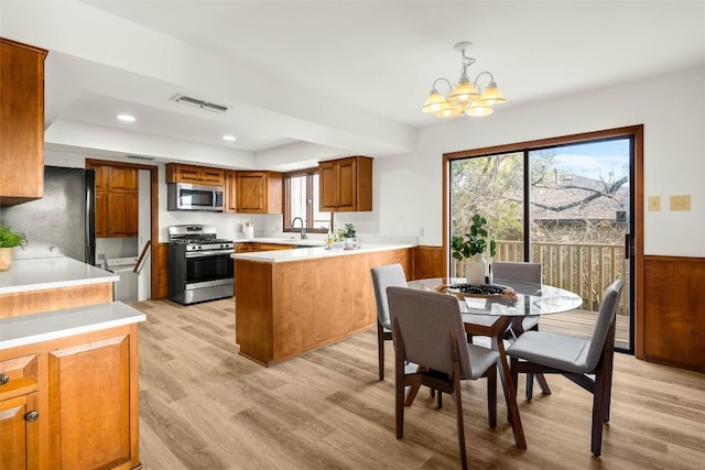 kitchen with stainless steel appliances, visible vents, brown cabinetry, wainscoting, and light wood-type flooring