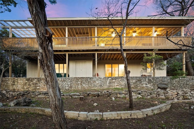 back of house at dusk featuring stone siding