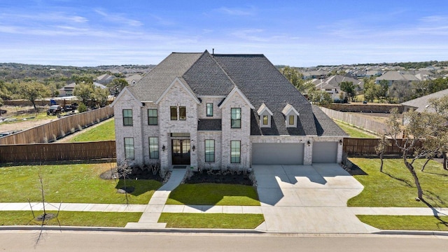 french country inspired facade featuring driveway, a front lawn, fence private yard, and brick siding