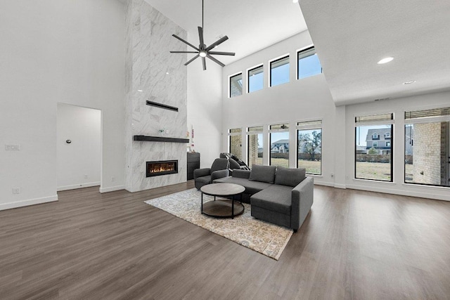 living area with ceiling fan, dark wood-style floors, baseboards, a fireplace, and a towering ceiling