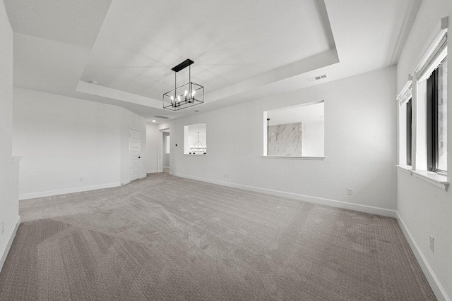spare room with light colored carpet, a chandelier, baseboards, visible vents, and a tray ceiling
