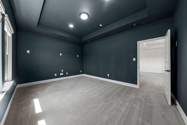 empty room with carpet, visible vents, a tray ceiling, and baseboards