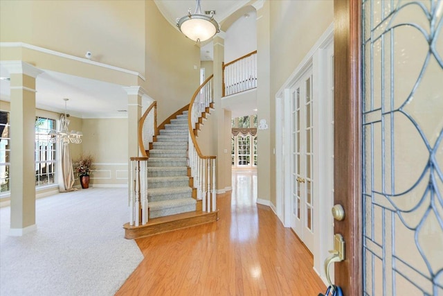 foyer entrance featuring light wood-style flooring, stairway, ornamental molding, ornate columns, and a notable chandelier