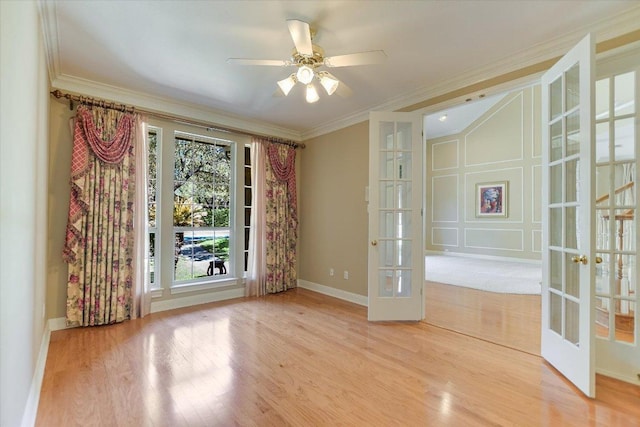 empty room featuring french doors, crown molding, light wood-style flooring, ceiling fan, and baseboards