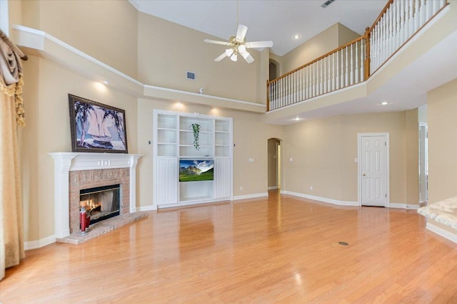 unfurnished living room featuring light wood finished floors, baseboards, arched walkways, a ceiling fan, and a brick fireplace