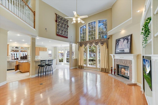 living room with a towering ceiling, light wood-type flooring, a fireplace, a ceiling fan, and ornate columns