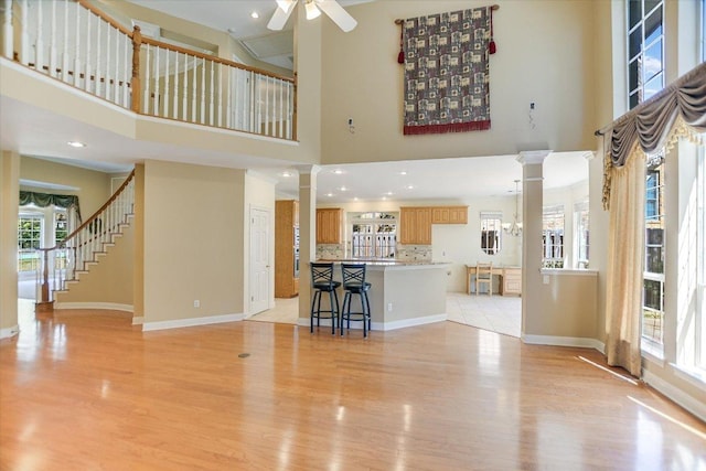 living area with ceiling fan, light wood-style flooring, a high ceiling, and ornate columns