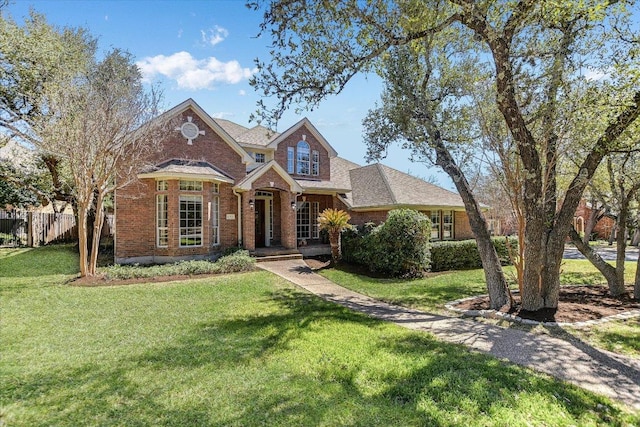 view of front of home featuring a shingled roof, a front yard, brick siding, and fence