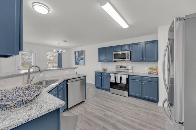 kitchen featuring a sink, appliances with stainless steel finishes, blue cabinetry, light stone countertops, and light wood finished floors