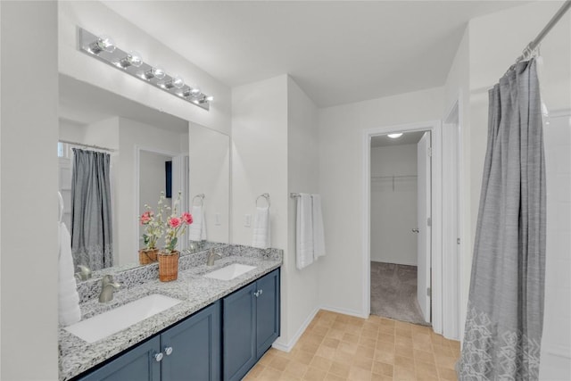 full bathroom featuring double vanity, a spacious closet, a sink, and baseboards