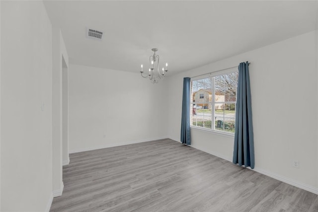 spare room featuring visible vents, light wood-style flooring, baseboards, and an inviting chandelier