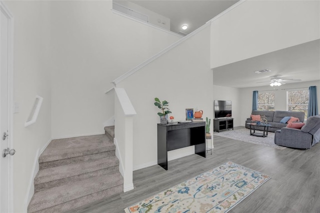 staircase featuring baseboards, visible vents, a ceiling fan, a towering ceiling, and wood finished floors