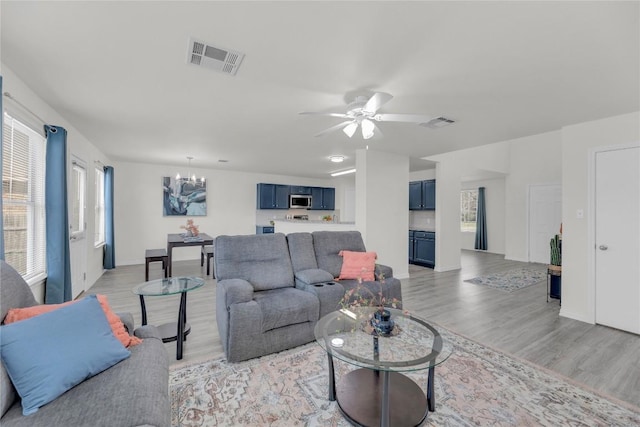 living area featuring light wood-style floors, visible vents, and ceiling fan with notable chandelier