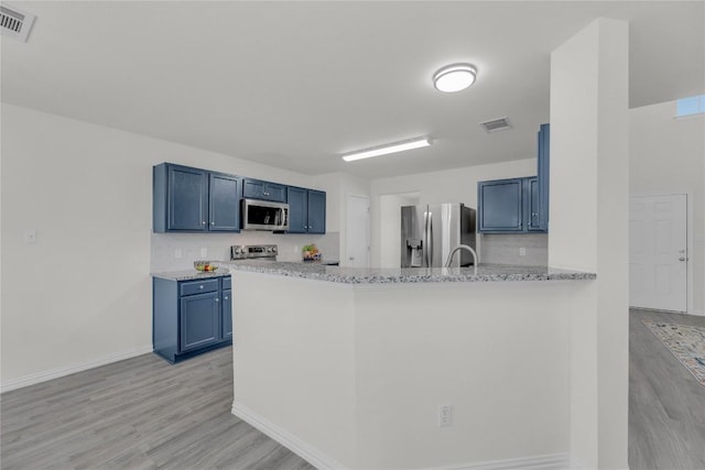 kitchen with a peninsula, light wood-style floors, appliances with stainless steel finishes, and blue cabinetry