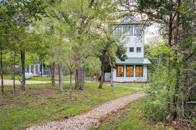 view of front of house with dirt driveway, metal roof, and a front lawn