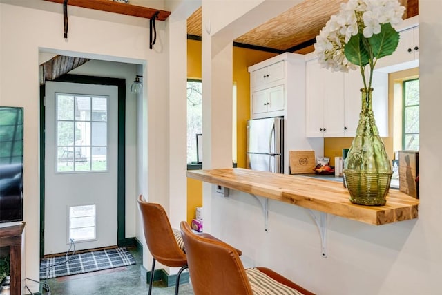 kitchen featuring finished concrete flooring, white cabinets, butcher block counters, a breakfast bar area, and stainless steel refrigerator