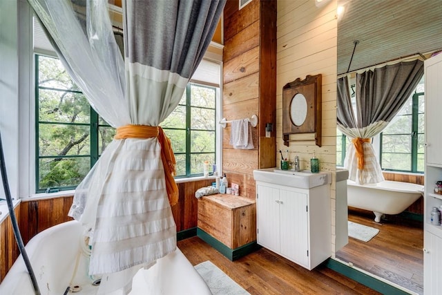 bathroom with wood walls, wood finished floors, vanity, a soaking tub, and plenty of natural light