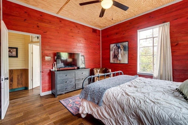 bedroom with a ceiling fan, wooden walls, and wood finished floors