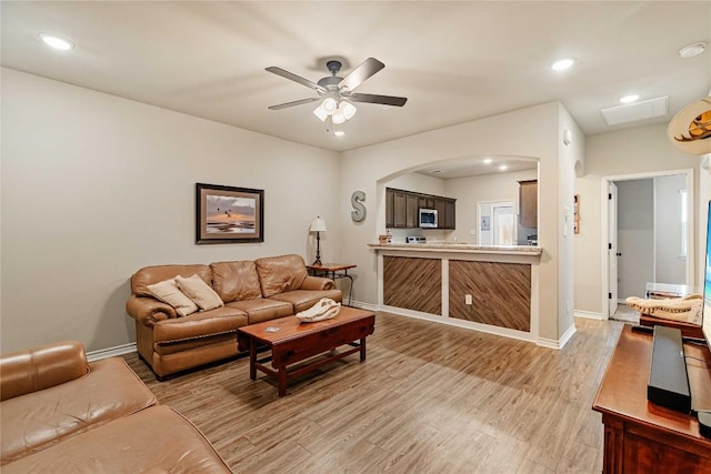 living room with light wood-style floors, arched walkways, baseboards, and a ceiling fan