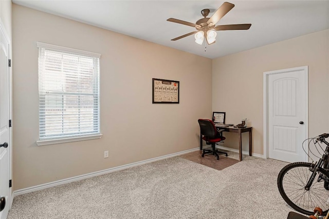 carpeted office space with a ceiling fan and baseboards