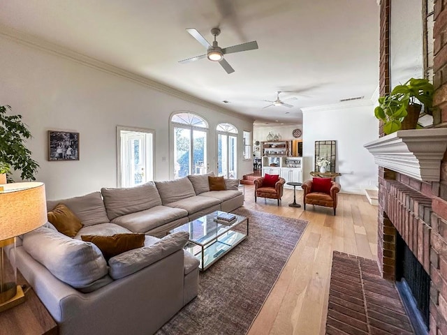 living room featuring hardwood / wood-style flooring, a fireplace, visible vents, a ceiling fan, and ornamental molding