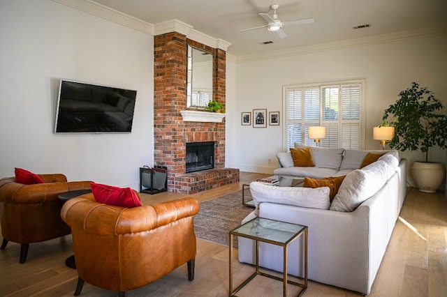 living area with a fireplace, visible vents, wood finished floors, and ornamental molding