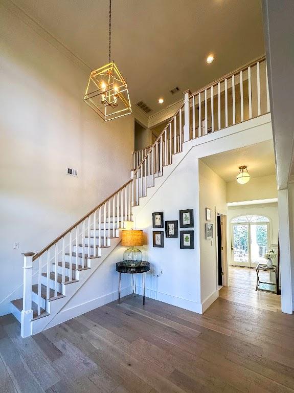 staircase featuring visible vents, hardwood / wood-style floors, a towering ceiling, and baseboards