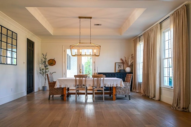 dining room with ornamental molding, a tray ceiling, visible vents, and hardwood / wood-style floors