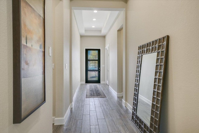 doorway to outside featuring wood finish floors, a raised ceiling, baseboards, and recessed lighting