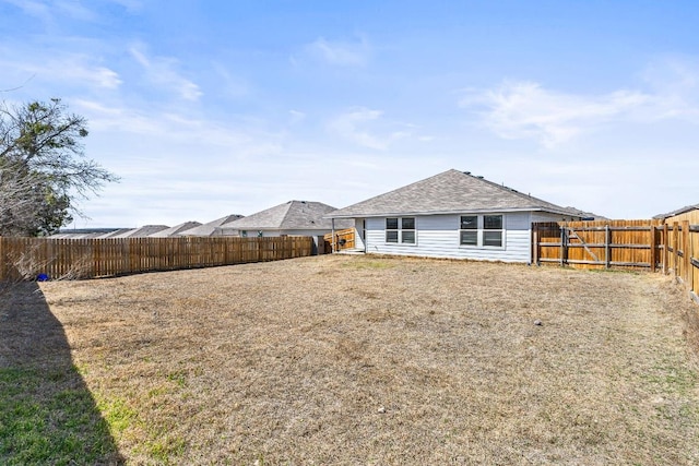 rear view of house featuring a fenced backyard and roof with shingles