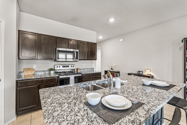 kitchen featuring appliances with stainless steel finishes, a kitchen bar, a sink, and light stone counters