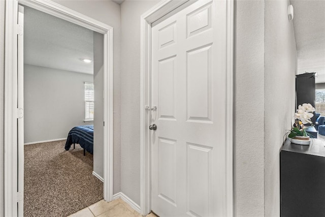 corridor with light tile patterned floors, baseboards, and light colored carpet