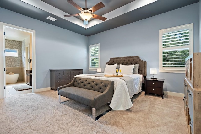 bedroom with visible vents, ensuite bathroom, a tray ceiling, baseboards, and light colored carpet