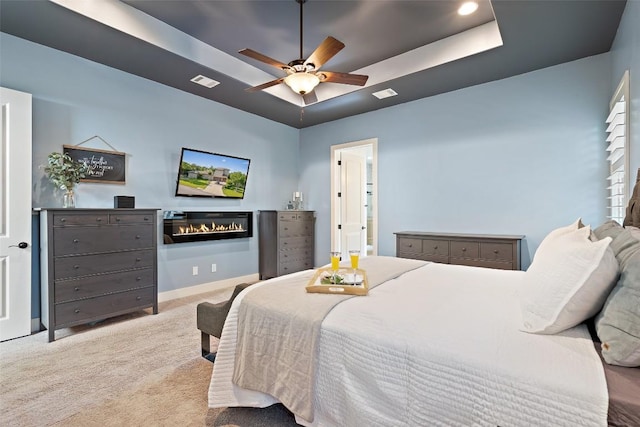 carpeted bedroom featuring visible vents, a raised ceiling, baseboards, and a glass covered fireplace