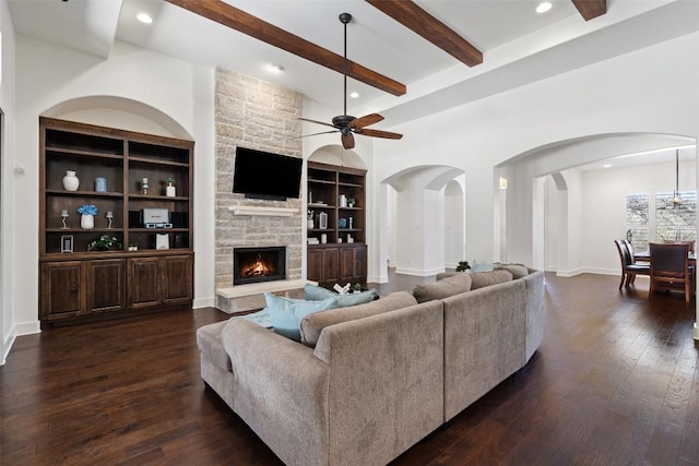 living room featuring dark wood-style floors, a stone fireplace, beam ceiling, and built in features