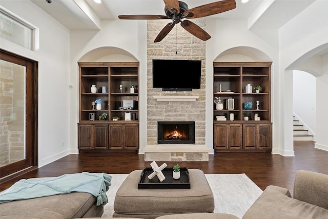 living area featuring baseboards, built in shelves, a stone fireplace, and wood finished floors