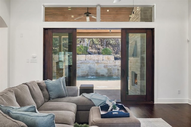 living area with baseboards, a fireplace, wood finished floors, arched walkways, and a ceiling fan