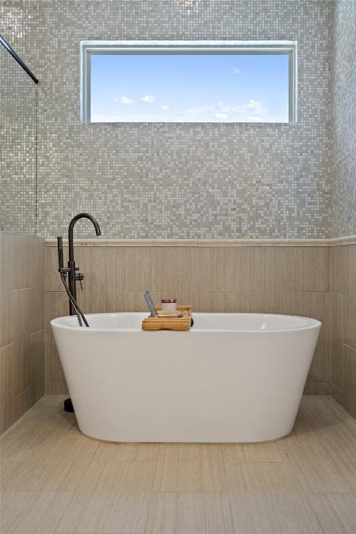 bathroom featuring a soaking tub, a healthy amount of sunlight, and tile walls