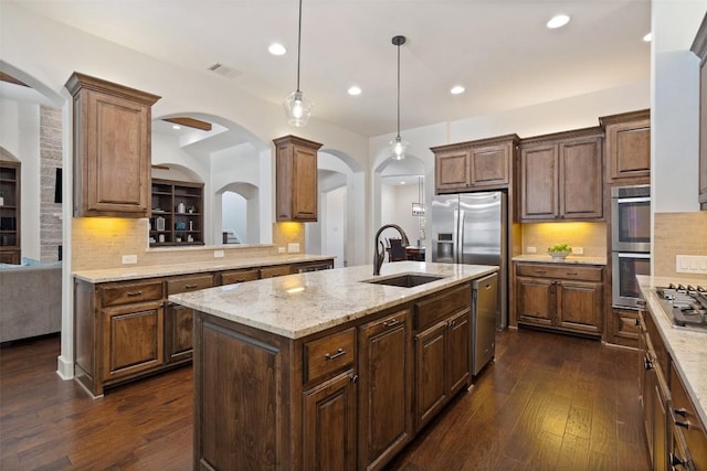 kitchen with dark wood-style floors, a center island with sink, light stone countertops, stainless steel appliances, and a sink