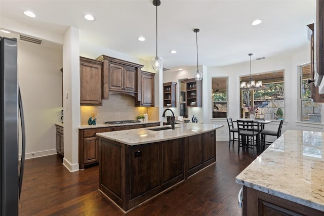 kitchen with a kitchen island with sink, a sink, tasteful backsplash, appliances with stainless steel finishes, and dark wood-style flooring