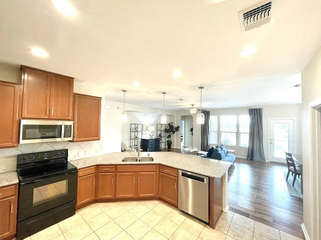 kitchen featuring stainless steel appliances, a peninsula, visible vents, open floor plan, and brown cabinets