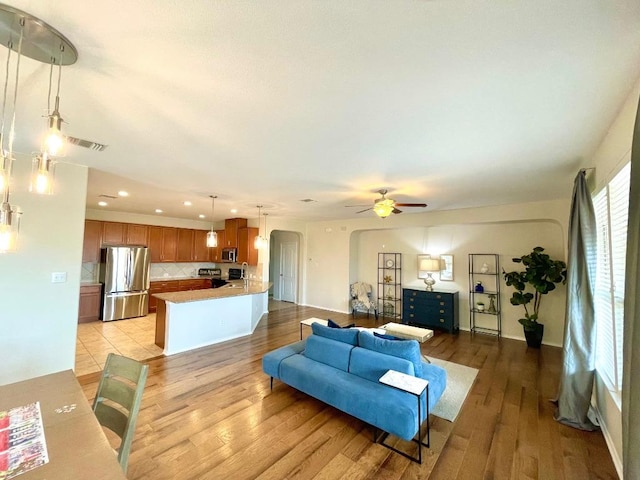 living room featuring a ceiling fan, arched walkways, visible vents, and light wood-style flooring