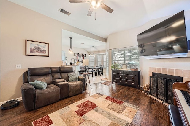 living room with a ceiling fan, a tile fireplace, wood-type flooring, and visible vents