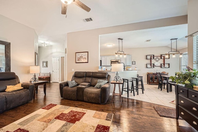 living room featuring ceiling fan with notable chandelier, light wood finished floors, lofted ceiling, and visible vents