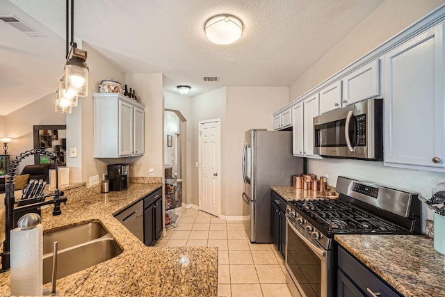 kitchen featuring light tile patterned floors, visible vents, light stone counters, hanging light fixtures, and stainless steel appliances