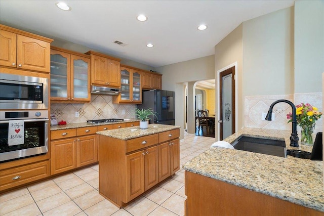 kitchen featuring light stone counters, under cabinet range hood, a sink, appliances with stainless steel finishes, and decorative columns