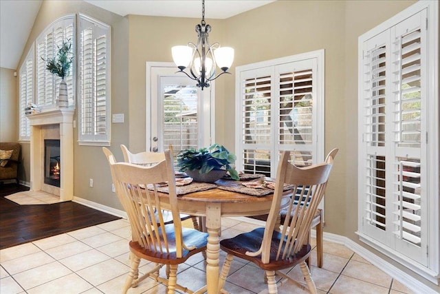 dining room with light tile patterned floors, a fireplace with flush hearth, baseboards, and an inviting chandelier