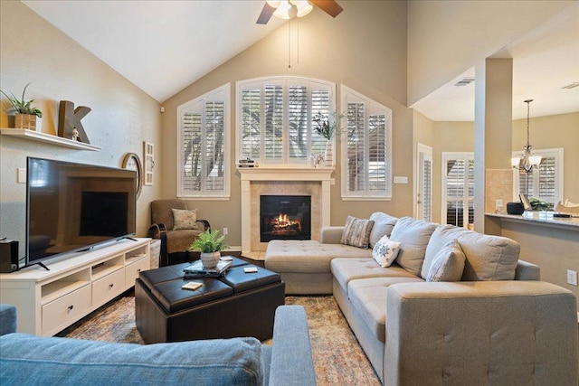 living room with high vaulted ceiling, ceiling fan with notable chandelier, visible vents, and a glass covered fireplace