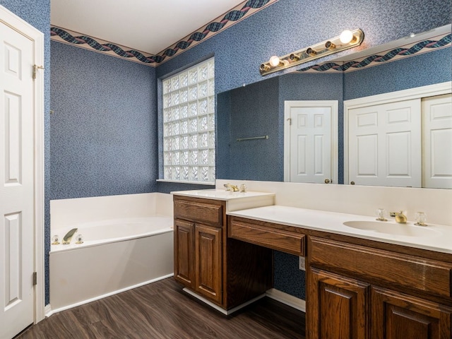 full bathroom with a bath, wallpapered walls, a sink, and wood finished floors