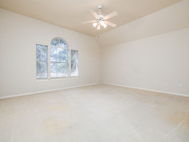 spare room with a ceiling fan, lofted ceiling, light colored carpet, and baseboards